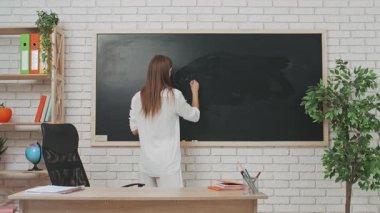 Okul öğretmeni sınıfta öğrencilere konuşuyor. Sınıftaki masada oturan genç bayan üniversite öğretmeni, tahtaya formül yazarak öğrencilere matematik dersi veriyor. Eğitim kavramı