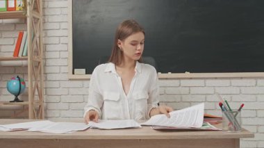 Okul öğretmeni sınıfta öğrencilere konuşuyor. Masadaki genç bayan üniversite öğretmeni masadaki öğrencilerin test kağıtlarını düzenleyen yazı tahtasının önünde. Eğitim kavramı.