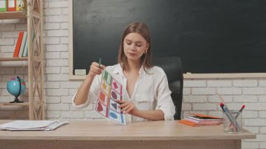 Okul öğretmeni sınıfta öğrencilere konuşuyor. Sınıftaki masada oturan genç bayan üniversite öğretmeni ilkokul çocuklarına dersi açıklıyor. Eğitim kavramı.