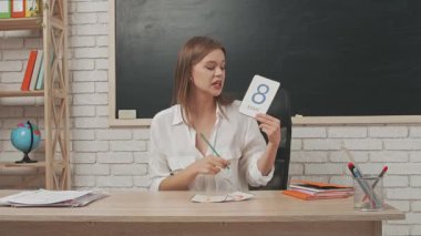 Okul öğretmeni sınıfta öğrencilere konuşuyor. Sınıftaki masada oturan genç bayan üniversite öğretmeni ilkokul çocuklarına dersi açıklıyor. Eğitim kavramı.