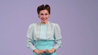 Klasik kıyafetli, çekici saç stili olan genç bir kadın mor stüdyo geçmişinde poz veriyor. Retro tarzında güzel bir aktris kamerada gerçekten mutludur. Güzellik ve eski tarz kavramı.