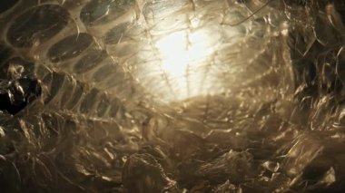 Şeffaf plastik bir yüzeyin, içinden ışık geçen karmaşık dokularını gösteren yakın plan bir resim. Macro, ağır çekim.