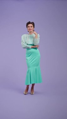 Klasik kıyafetli, çekici saç stili olan genç bir kadın mor stüdyo geçmişinde poz veriyor. Retro tarzında güzel bir aktris kameraya hava öpücüğü veriyor. Güzellik ve eski tarz konsept.