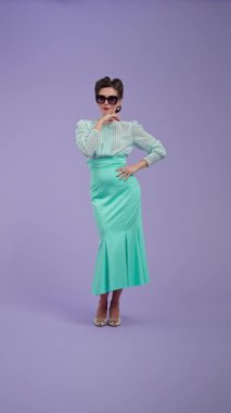 Klasik kıyafetli, çekici saç stili olan genç bir kadın mor stüdyo geçmişinde poz veriyor. Eski tarz güzel bir aktris gözlük takar ve güzel poz verir. Güzellik ve eski tarz konsept.