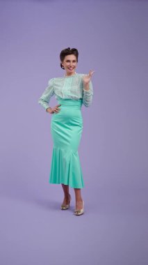 Klasik kıyafetli, çekici saç stili olan genç bir kadın mor stüdyo geçmişinde poz veriyor. Retro tarzında güzel bir aktris kamerada mutlu bir şekilde anlatıyor. Güzellik ve eski tarz konsept.