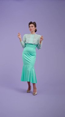 Klasik kıyafetli, çekici saç stili olan genç bir kadın mor stüdyo geçmişinde poz veriyor. Retro tarzında güzel bir aktris kamerada mutlu bir şekilde anlatıyor. Güzellik ve eski tarz konsept.