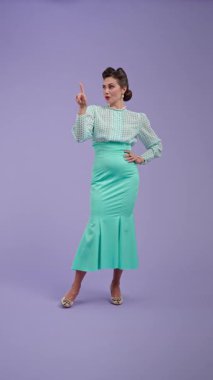 Klasik kıyafetli, çekici saç stili olan genç bir kadın mor stüdyo geçmişinde poz veriyor. Retro tarzında güzel bir aktris, parmağını kameraya doğrultuyor. Güzellik ve eski tarz konsept