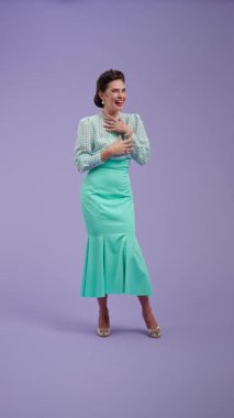 Klasik kıyafetli, çekici saç stili olan genç bir kadın mor stüdyo geçmişinde poz veriyor. Retro tarzında güzel bir aktris samimi mutluluğu ifade ederek gülüyor. Güzellik ve eski tarz konsept.