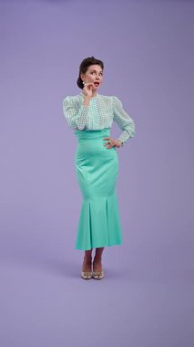 Klasik kıyafetli, çekici saç stili olan genç bir kadın mor stüdyo geçmişinde poz veriyor. Retro tarzında güzel bir aktris sırlara kulak misafiri olur ve ironik bir şekilde güler. Güzellik ve eski tarz konsept.