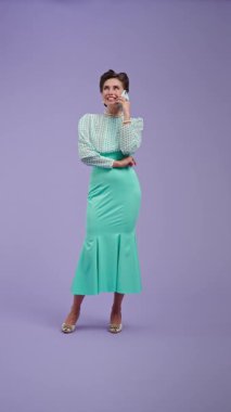 Mor stüdyo arka planında çekici saç stili olan klasik kıyafetli genç bir kadın. Retro tarzında güzel bir aktris telefonda keyifli bir şekilde konuşuyor. Güzellik ve eski tarz konsept.