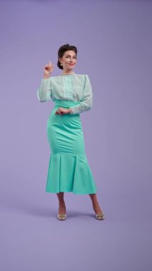 Mor stüdyo arka planında çekici saç stili olan klasik kıyafetli genç bir kadın. Retro tarzında güzel bir aktris parmağıyla işaret ediyor. Güzellik ve eski tarz konsept.