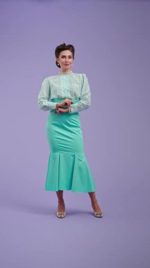 Mor stüdyo arka planında çekici saç stili pozları olan klasik kıyafetli genç bir kadın. Eski moda modunda güzel bir aktris parmağını yana doğru gösteriyor. Güzellik ve eski tarz konsept.