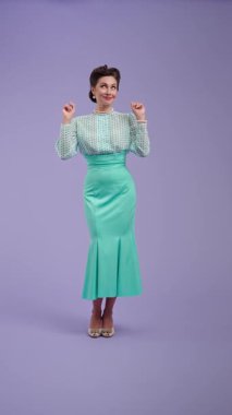 Mor stüdyo arka planında çekici saç stili pozları olan klasik kıyafetli genç bir kadın. Eski tarz bir aktris, ellerinde sevgi olan kalbi gösterir ve yukarı doğru puan verir. Güzellik ve eski tarz konsept.