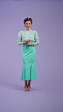 Mor stüdyo arka planında çekici saç stili pozları olan klasik kıyafetli genç bir kadın. Eski tarz bir aktris, ellerinde sevgi olan kalbi gösterir ve yukarı doğru puan verir. Güzellik ve eski tarz konsept.