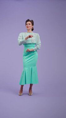 Mor stüdyo arka planında çekici saç stili pozları olan klasik kıyafetli genç bir kadın. Eski moda modunda güzel bir aktris parmağını yana doğru gösteriyor. Güzellik ve eski tarz konsept.