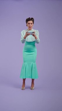 Klasik kıyafetli, çekici saç stili olan genç bir kadın mor stüdyo geçmişinde poz veriyor. Retro tarzında güzel bir aktris telefonda oyun oynuyor ve kaybediyor. Güzellik ve eski tarz konsept.