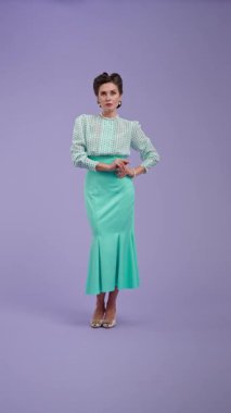 Klasik kıyafetli, çekici saç stili olan genç bir kadın mor stüdyo geçmişinde poz veriyor. Kamerada retro tarzı dönüşler yapan güzel bir aktris. Güzellik ve eski tarz konsept.