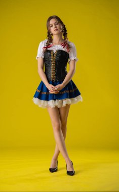 Genç bir kadın geleneksel bir kostümle poz veriyor. Parlak sarı bir fonda korse ve etek var..