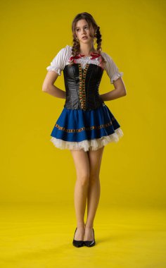 Genç bir kadın geleneksel bir kostümle poz veriyor. Parlak sarı bir fonda korse ve etek var..