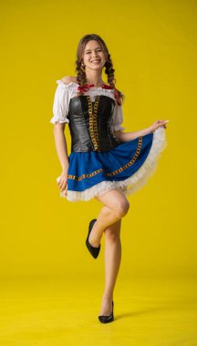 Geleneksel folklorik giyinmiş bir kadın canlı sarı bir arka plana karşı poz verir, kültürel çekiciliği ve zarafeti somutlaştırır..