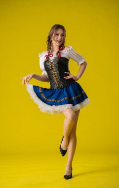 Geleneksel folklorik giyinmiş bir kadın canlı sarı bir arka plana karşı poz verir, kültürel çekiciliği ve zarafeti somutlaştırır..