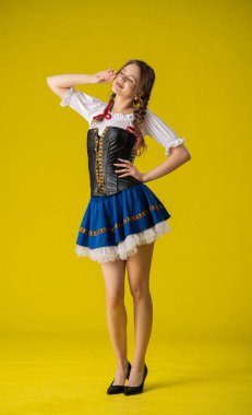 Geleneksel folklorik giyinmiş bir kadın canlı sarı bir arka plana karşı poz verir, kültürel çekiciliği ve zarafeti somutlaştırır..