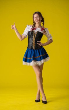 Mavi ve beyaz geleneksel Bavyera kostümü giymiş bir kadın, parlak sarı bir arka plana karşı güvenle poz verir..