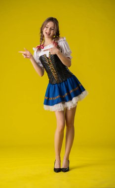 Renkli, geleneksel kostümlü genç bir kadın canlı, sarı bir arka plana karşı poz veriyor, neşe saçıyor..