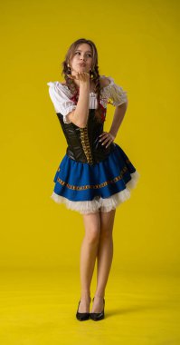 Geleneksel bir kostümle poz veren bir kadın, bir öpücük yolluyor, parlak sarı bir arka plana kurulmuş..