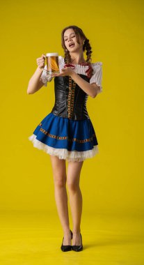 Geleneksel giyinmiş bir kadın, parlak sarı bir arka planda duran büyük bir kupa biranın keyfini çıkarıyor..