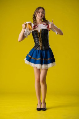 Geleneksel Bavyera elbisesi giymiş, elinde bira bardağıyla gülümseyen genç bir kadın..