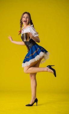 Geleneksel giyinmiş bir kadın, parlak sarı bir arka planda duran büyük bir kupa biranın keyfini çıkarıyor..