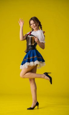 Geleneksel giyinmiş bir kadın, parlak sarı bir arka planda duran büyük bir kupa biranın keyfini çıkarıyor..