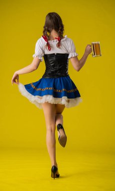 Geleneksel giyinmiş bir kadın, parlak sarı arka planda büyük bir bardak biranın keyfini çıkarıyor. Arka plan