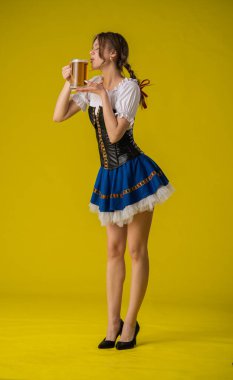 Bavyera kıyafetli genç bir kadın canlı sarı bir arka planda bira bardağının keyfini çıkarıyor. Neşeli ve canlı bir atmosfer..