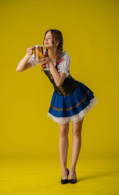 Bavyera kıyafetli genç bir kadın canlı sarı bir arka planda bira bardağının keyfini çıkarıyor. Neşeli ve canlı bir atmosfer..