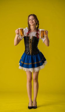 Geleneksel kıyafetli genç bir kadın iki bira bardağı tutuyor, parlak sarı bir fona gülümsüyor..