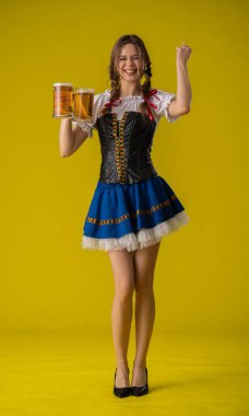 Geleneksel Bavyera kıyafeti giymiş, elinde bira bardakları olan neşeli genç bir kadın neşeli bir şekilde kutlama yapıyor..