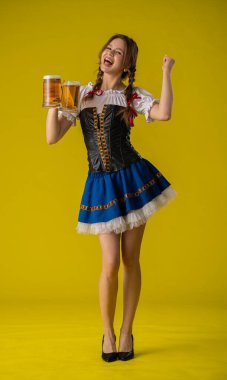 Geleneksel Bavyera kıyafeti giymiş, elinde bira bardakları olan neşeli genç bir kadın neşeli bir şekilde kutlama yapıyor..