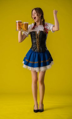 Canlı, geleneksel elbiseli neşeli genç bir kadın iki bardak bira kaldırıyor, kutlama ve neşe ifade ediyor..