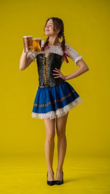 Geleneksel kıyafetli genç bir kadın iki bira bardağı tutuyor, parlak sarı bir fona gülümsüyor..