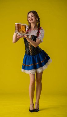 Geleneksel kıyafetli genç bir kadın iki bira bardağı tutuyor, parlak sarı bir fona gülümsüyor..