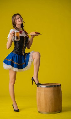 Geleneksel kıyafetli bir kadın bir bardak bira ve bir tabak yemek taşır, bir ayağı fıçının üzerinde durur..
