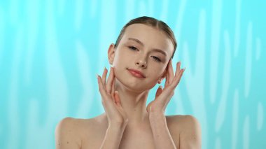 Açık tenli genç bir kadın nazikçe yüzüne dokunuyor, cilt teması ve gençlik ışıltısı öneriyor..