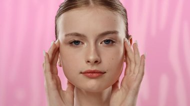 Açık tenli genç bir kadın nazikçe yüzüne dokunuyor, cilt teması ve gençlik ışıltısı öneriyor..