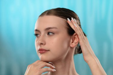 Açık tenli genç bir kadın nazikçe yüzüne dokunuyor, cilt teması ve gençlik ışıltısı öneriyor..