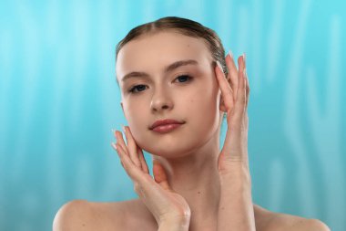 Açık tenli genç bir kadın nazikçe yüzüne dokunuyor, cilt teması ve gençlik ışıltısı öneriyor..