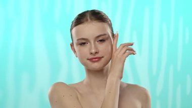 Açık tenli genç bir kadın nazikçe yüzüne dokunuyor, cilt teması ve gençlik ışıltısı öneriyor..