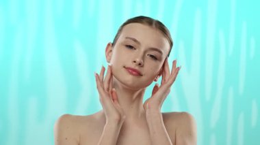 Açık tenli genç bir kadın nazikçe yüzüne dokunuyor, cilt teması ve gençlik ışıltısı öneriyor..