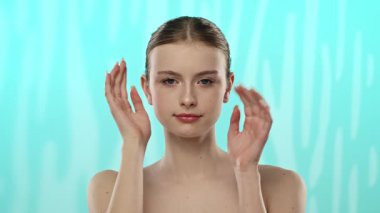 Açık tenli genç bir kadın nazikçe yüzüne dokunuyor, cilt teması ve gençlik ışıltısı öneriyor..